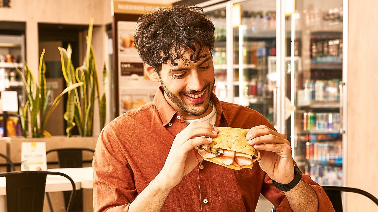 Hombre sentado y disfrutando un sándwich en Shell Select