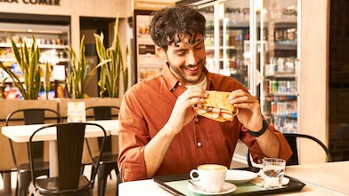 Hombre sentado y disfrutando un sándwich en Shell Select