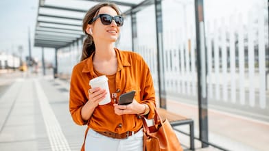 Chica parada usando su celular mientras toma un café