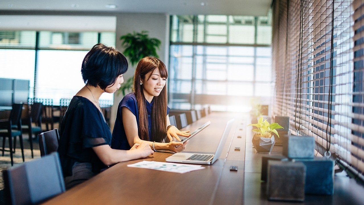 Dos mujeres sentadas en un escritorio mirando una computadora y una tablet
