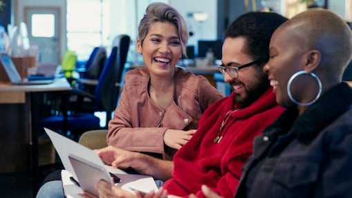 Tres personas en una oficina sentados juntos, mirando papeles y riendo