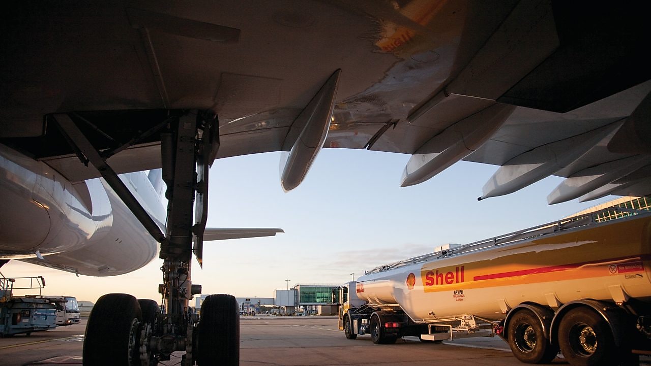 Vista de un camión de Shell por debajo del ala de un avión en la pista de aterrizaje