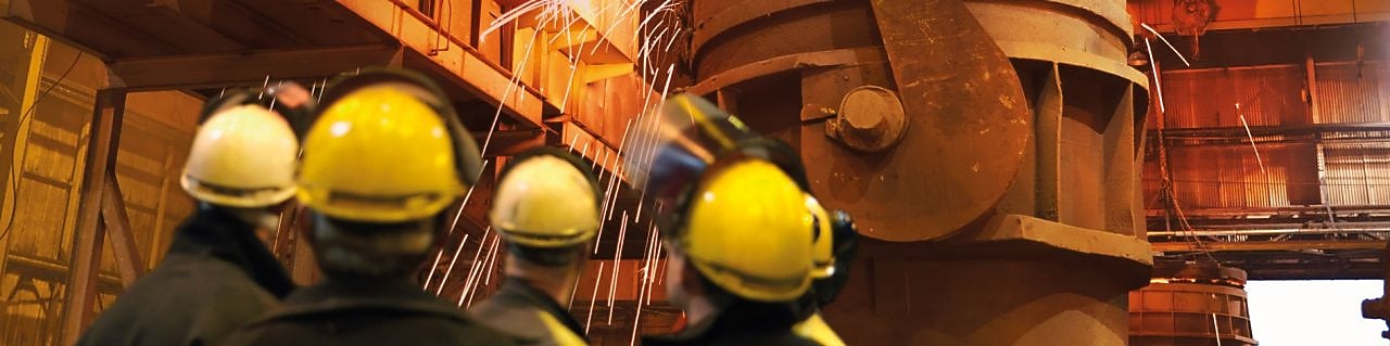 trabajadores mirando maquinaria pesada en una planta de procesamiento de metales