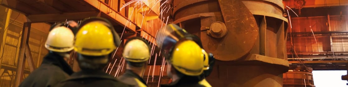 trabajadores mirando maquinaria pesada en una planta de procesamiento de metales