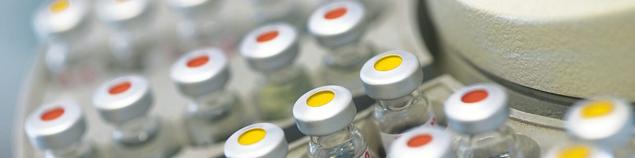 Filas de frascos de medicamentos en un soporte, algunas de ellas con puntos rojos y otras con puntos amarillos en la tapa