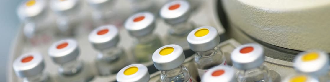 Filas de frascos de medicamentos en un soporte, algunas de ellas con puntos rojos y otras con puntos amarillos en la tapa