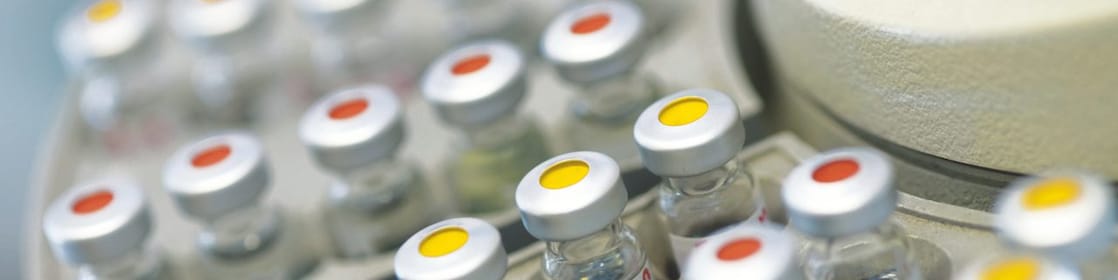 Filas de frascos de medicamentos en un soporte, algunas de ellas con puntos rojos y otras con puntos amarillos en la tapa