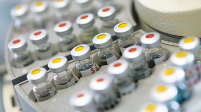 Filas de frascos de medicamentos en un soporte, algunas de ellas con puntos rojos y otras con puntos amarillos en la tapa