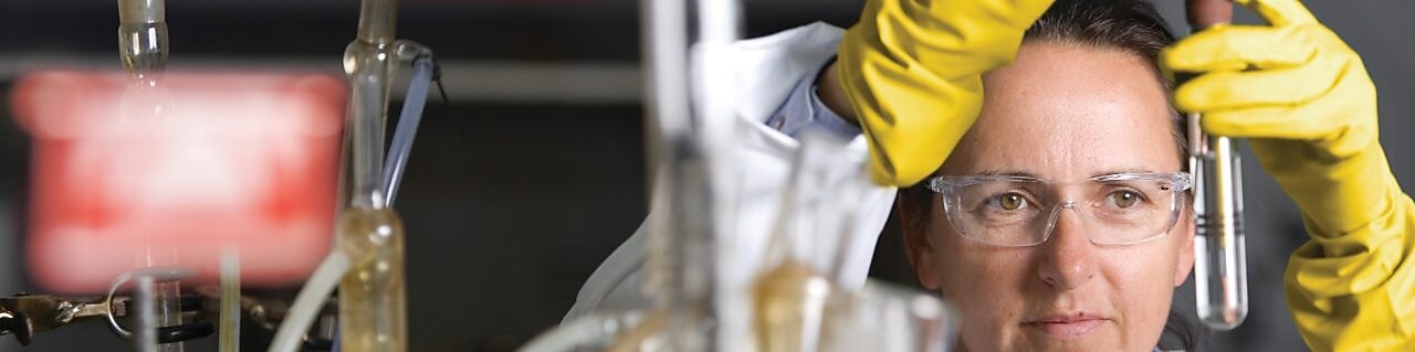 mujer con lentes de seguridad llevando a cabo un experimento de laboratorio