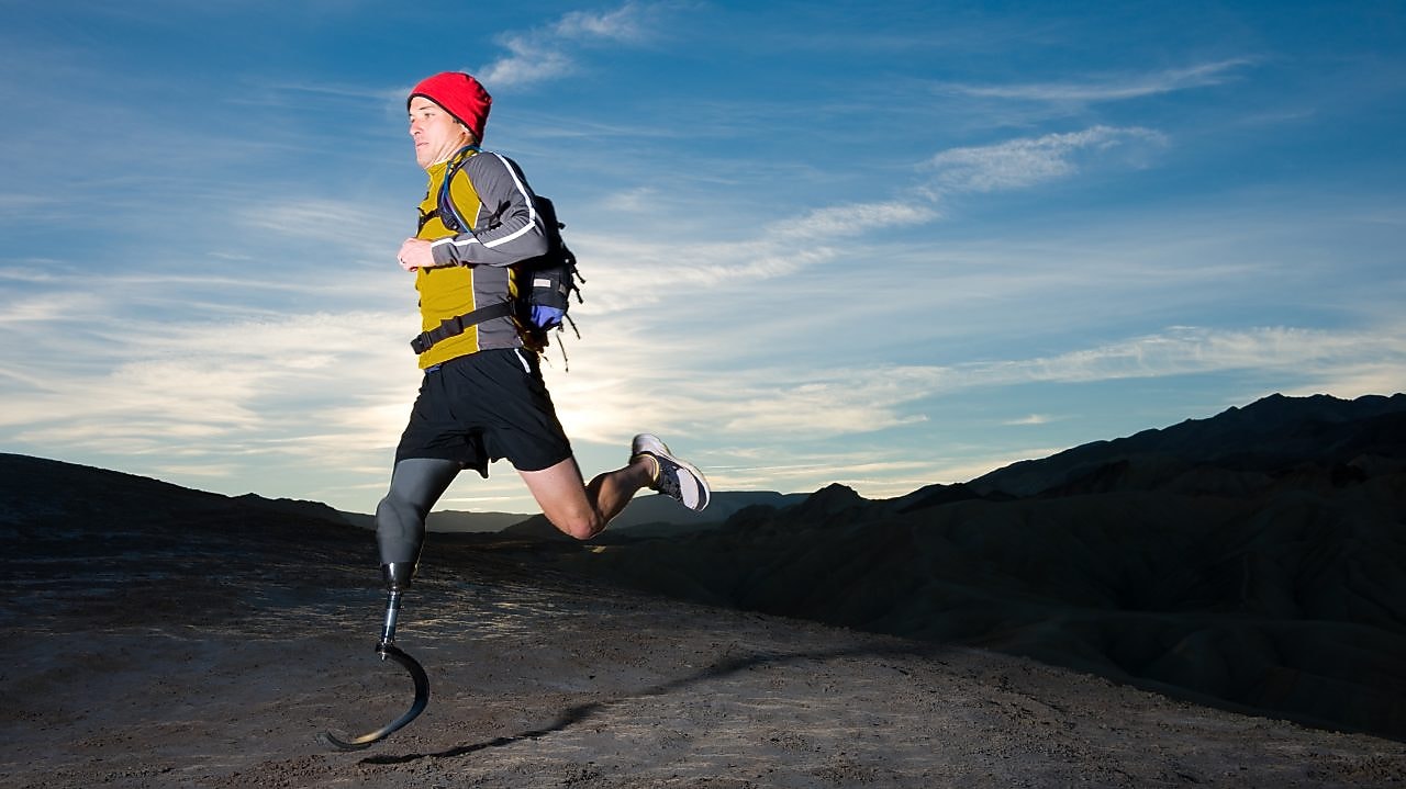 Man with prosthetic leg, in running clothes, running in the hills in the early morning