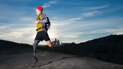 Man with prosthetic leg, in running clothes, running in the hills in the early morning