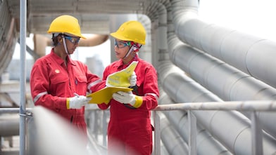 operarios en mamelucos rojos y cascos amarillos leyendo un manual en una fábrica