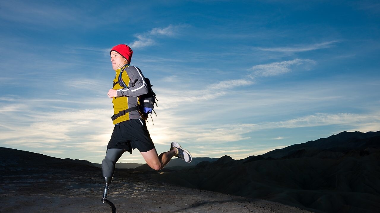 man with prosthetic leg, in running clothes, running in the hills in the early morning