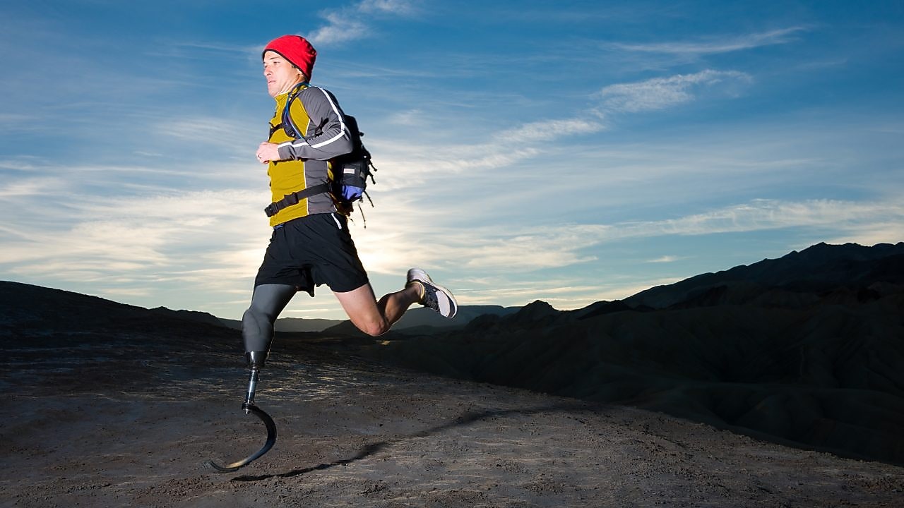 man with prosthetic leg, in running clothes, running in the hills in the early morning