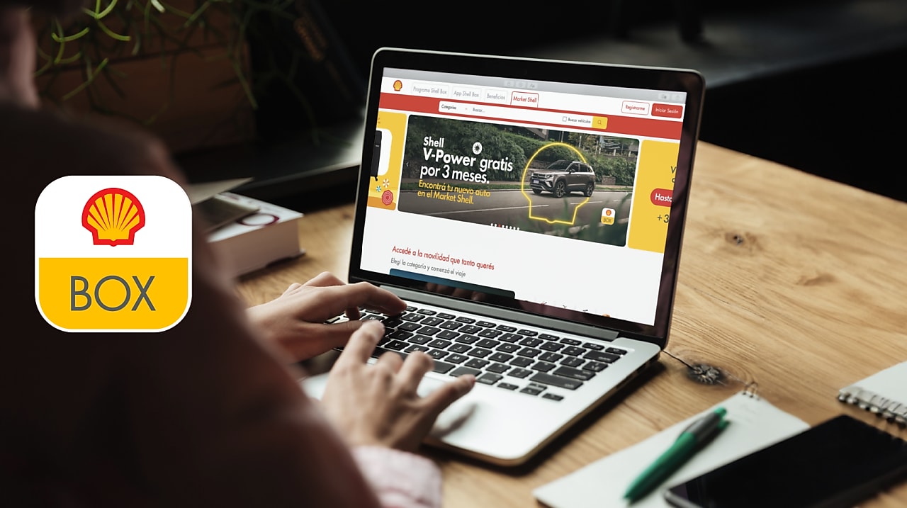 Computadora abierta sobre un escritorio y persona de espaldas tipeando sobre el teclado.