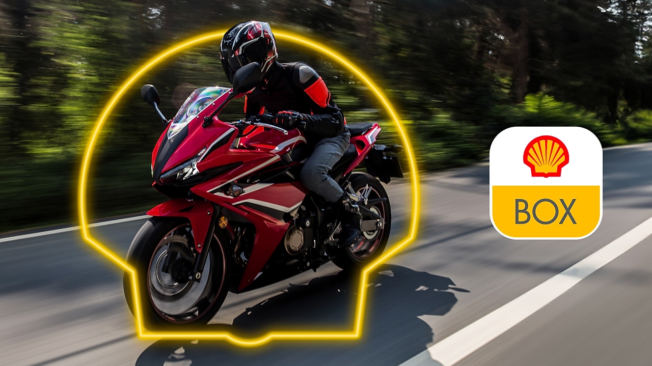 Moto rodando por una avenida, se ve el logo de Shell en neón alrededor del auto