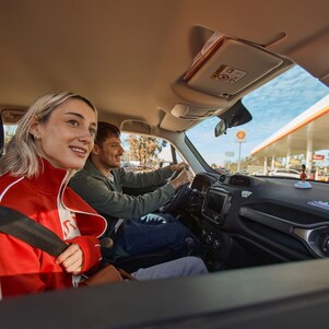 chica que está en un auto con otro chico entrando a una estación Shell