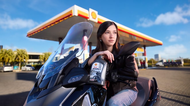 Chica sentada delante de moto con una botella de Shell Advance en sus manos.