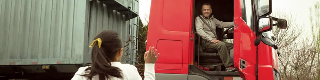Hombre en una cabina roja de camión con la puerta abierta despidiéndose de su hija