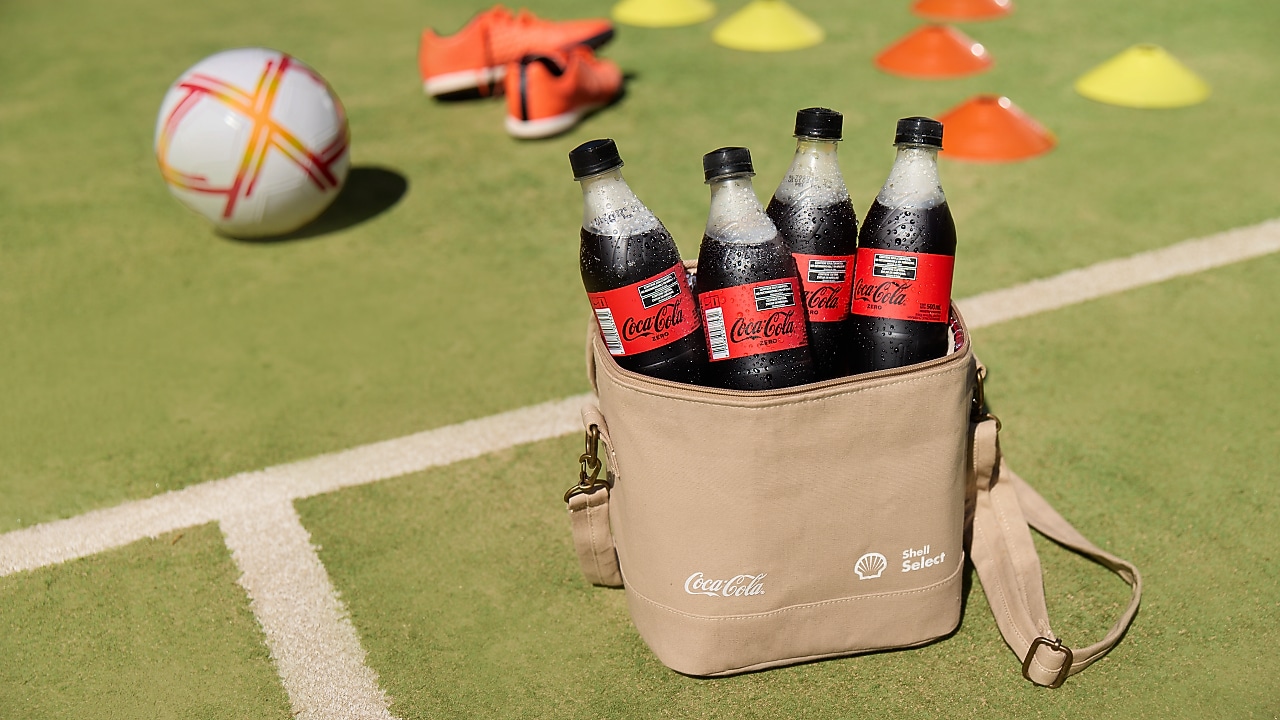 Bolso cooler con botellas de Coca-Cola dentro, posando sobre una cancha de pasto sintético.