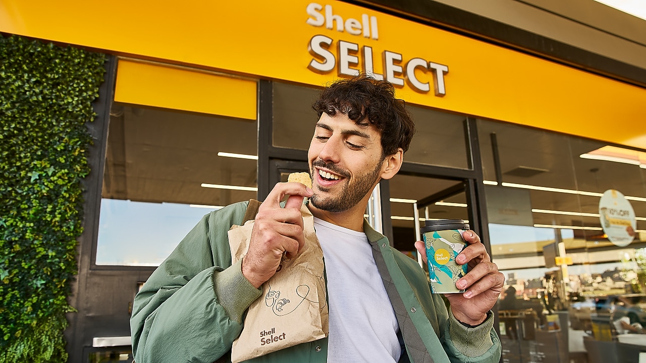 Hombre saliendo de Shell Select con medialuna y café