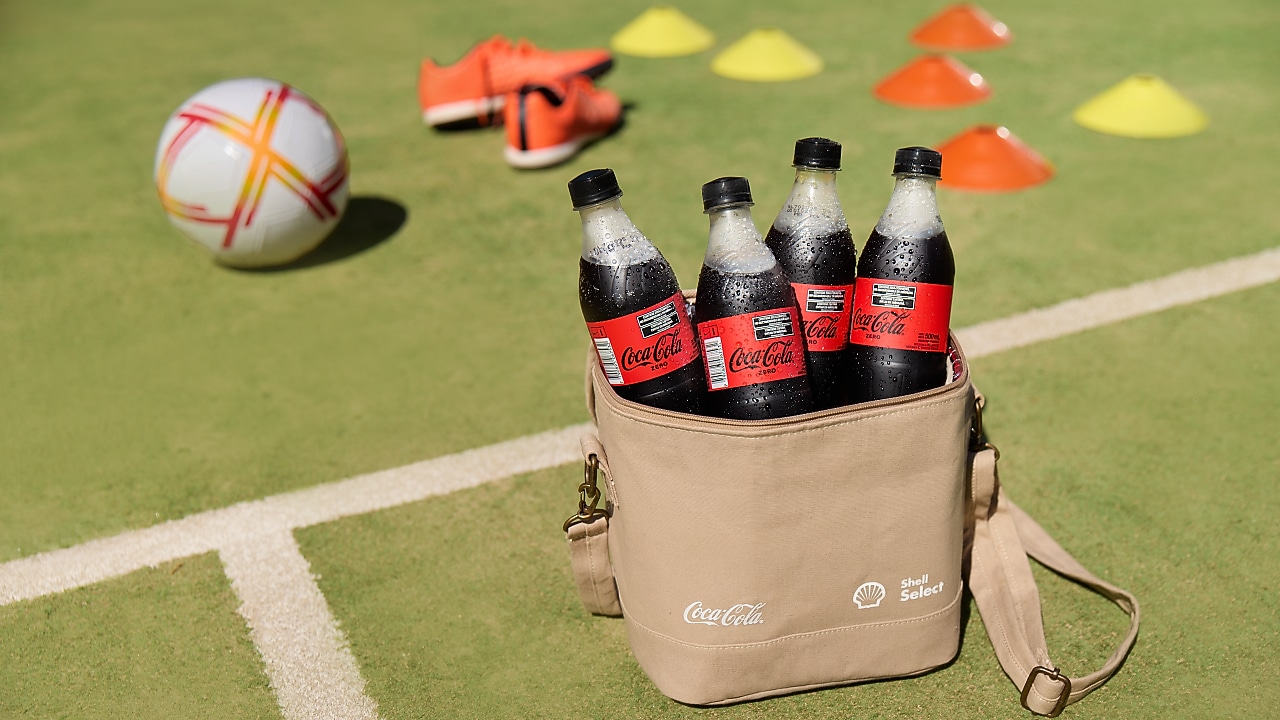 Bolso cooler con botellas de Coca-Cola dentro, posando sobre una cancha de pasto sintético.