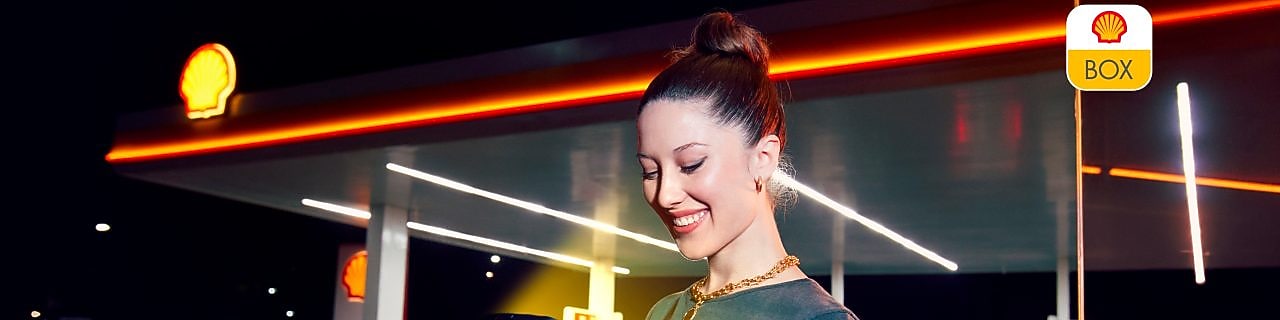 Mujer parada en una Shell y usando su celular.