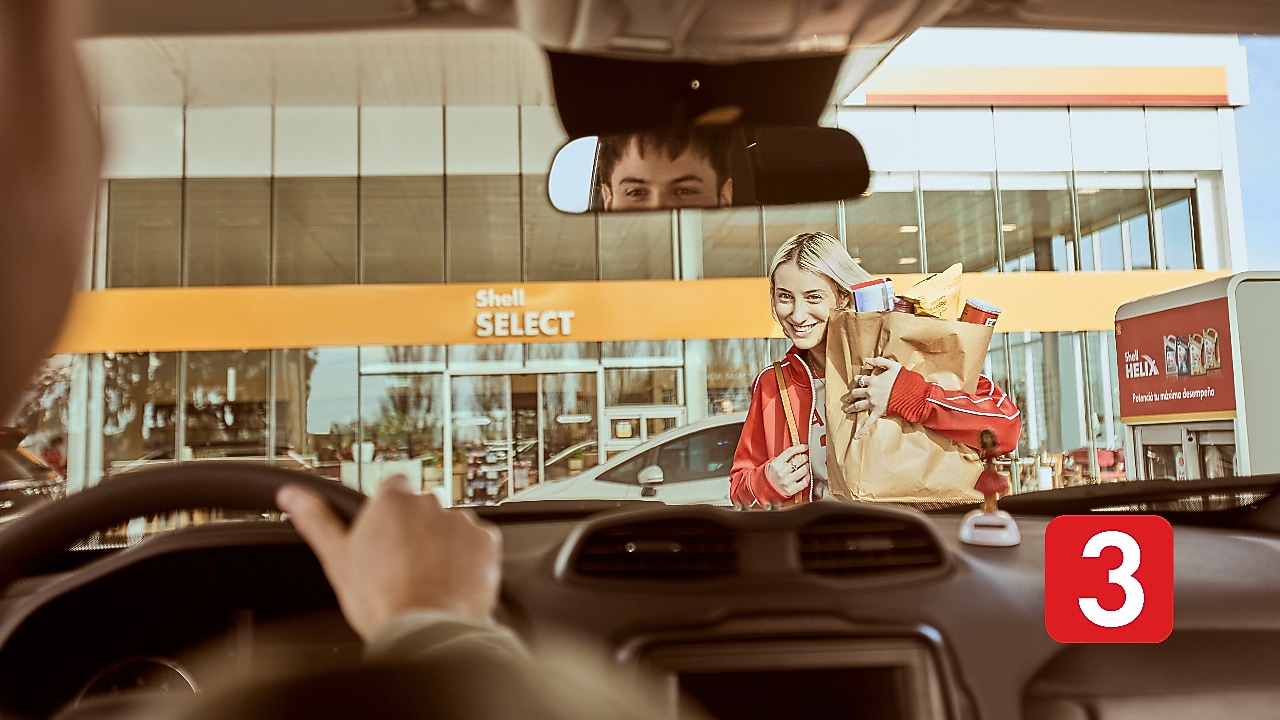 Mujer volviendo a su auto luego de comprar comida en Shell Select.