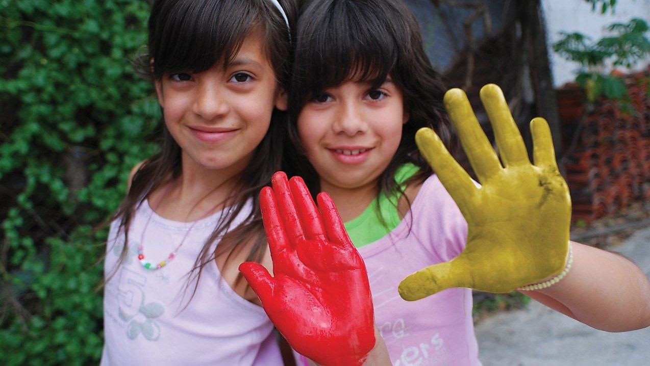 Dos niñas mostrando sus manos cubiertas de témpera