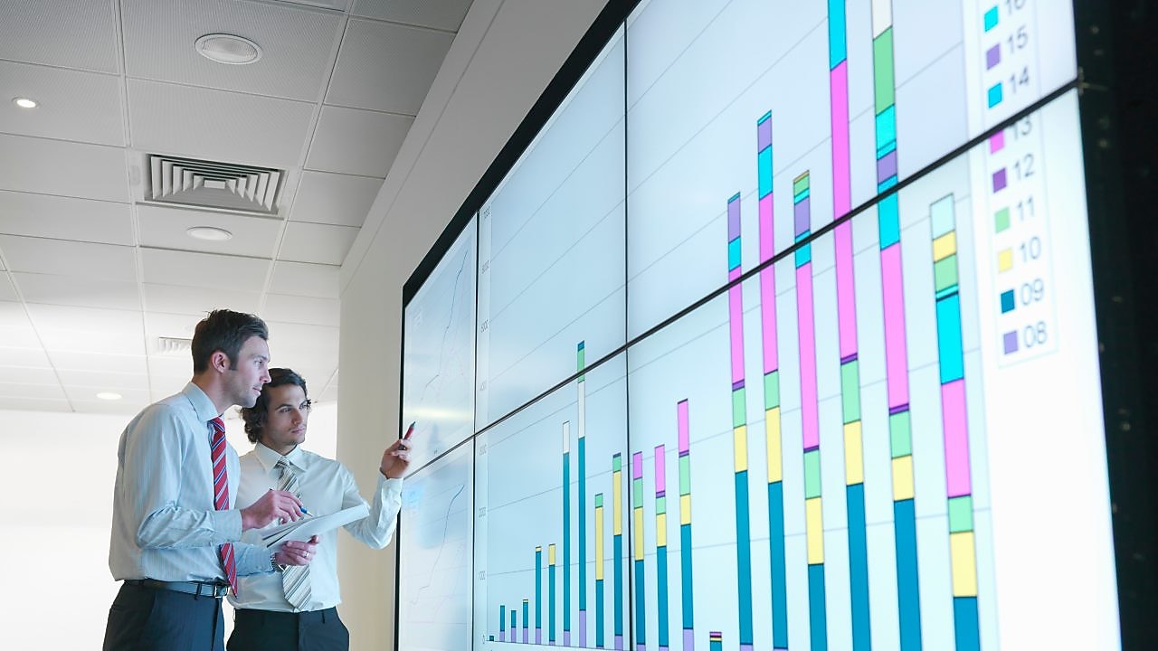 Hombres de negocios analizan informes visualizados en una gran pantalla digital