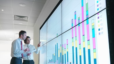 Hombres de negocios analizan informes visualizados en una gran pantalla digital