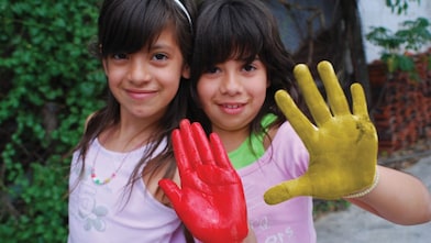 Dos niñas mostrando sus manos cubiertas de témpera