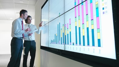 Hombres de negocios analizan informes visualizados en una gran pantalla digital