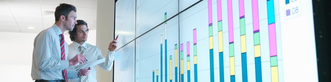 Hombres de negocios analizan informes visualizados en una gran pantalla digital