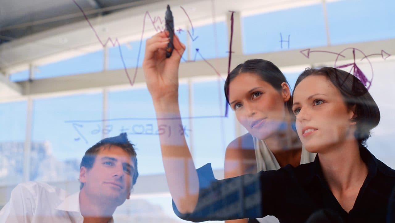 Mujer de negocios dibujando gráficos en una pizarra transparente