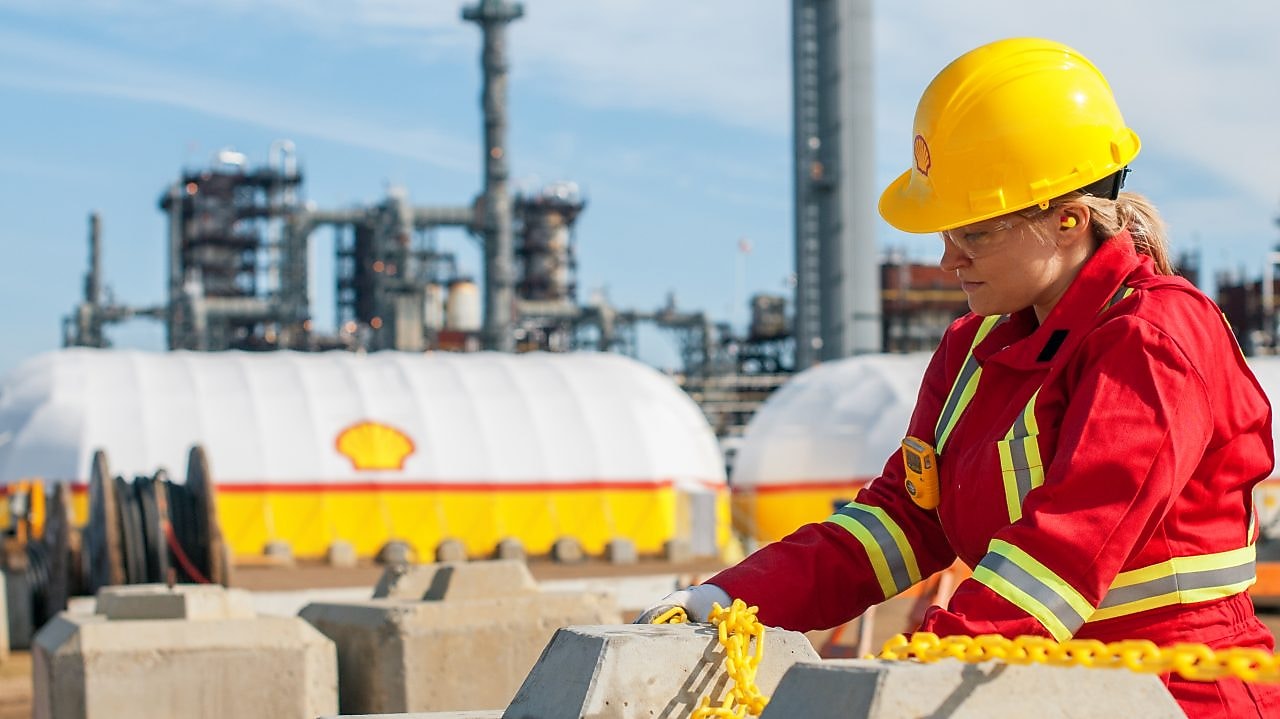Mujer con el traje rojo de shell trabajando en una refinería.